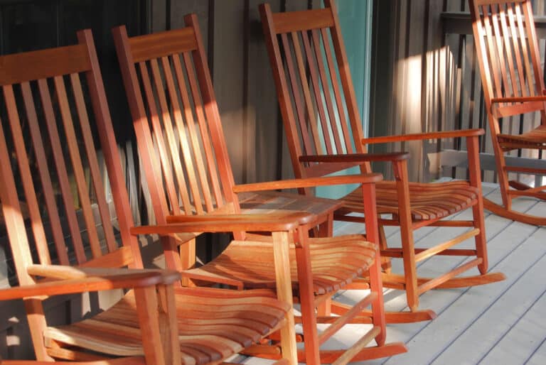 Wooden rocking chairs lined up on a cabin porch overlooking trees