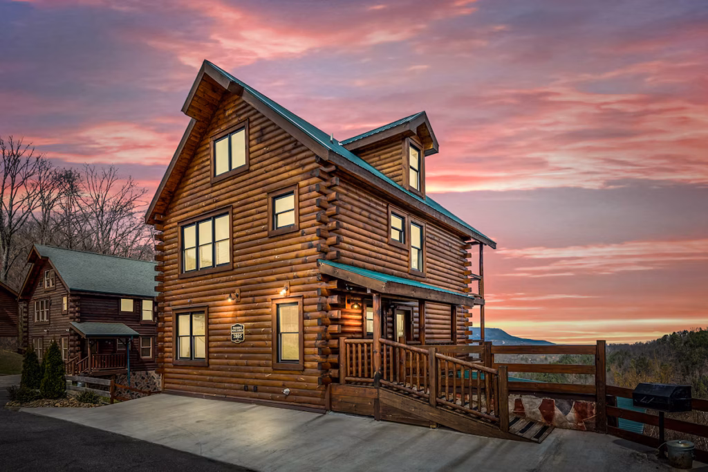 Log cabin with a green metal roof and wraparound deck at sunset with Smoky Mountain views — Your Stellar Stay, Tennessee